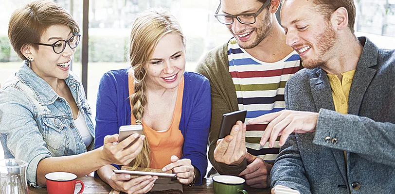 Four people at a table sharing smartphone content and smiling.