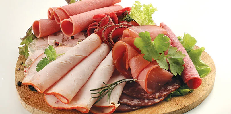Assorted deli meats on a wooden platter with herbs and greens.